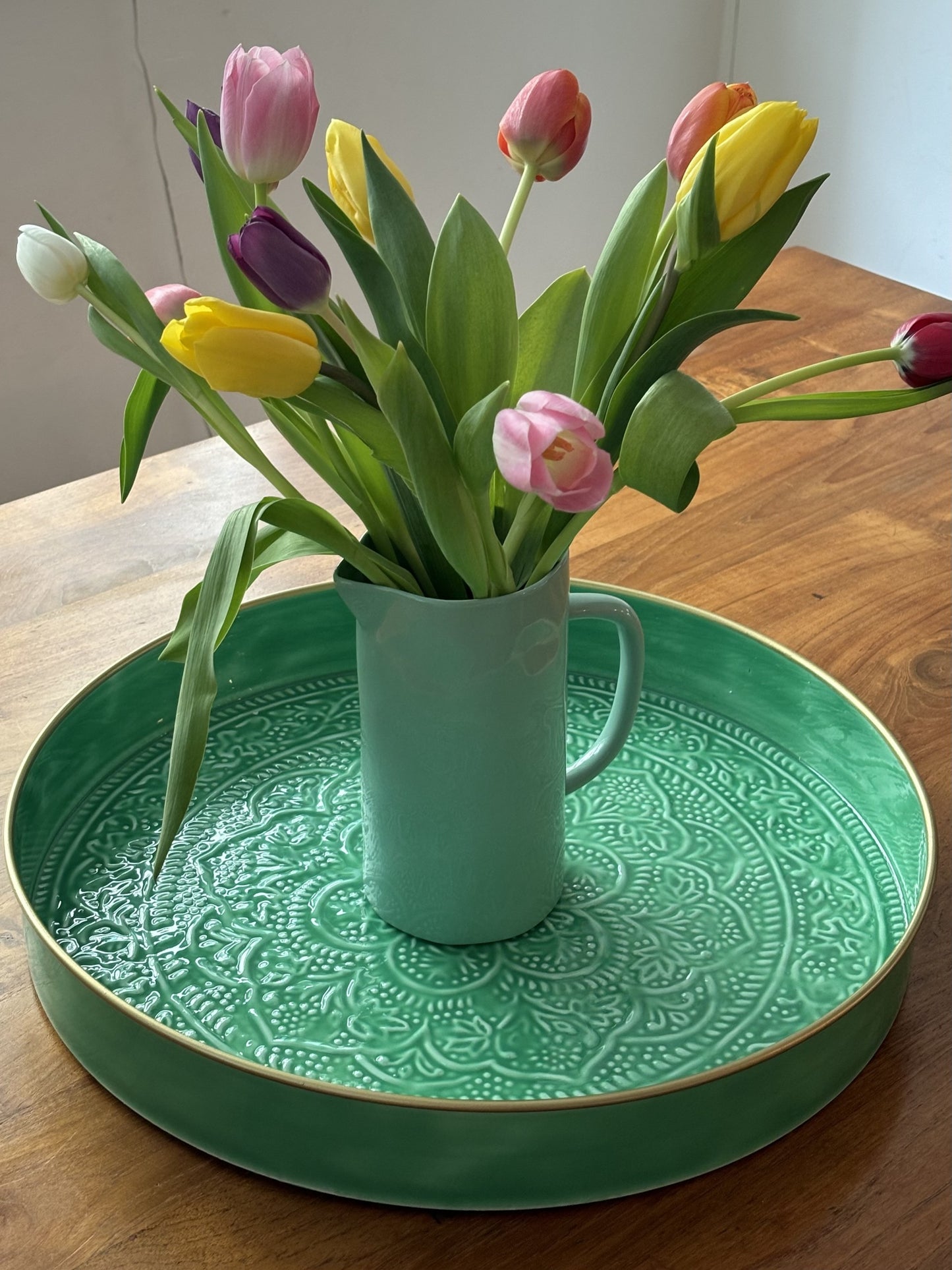 A mint coloured jug filled with tulips on a green tray