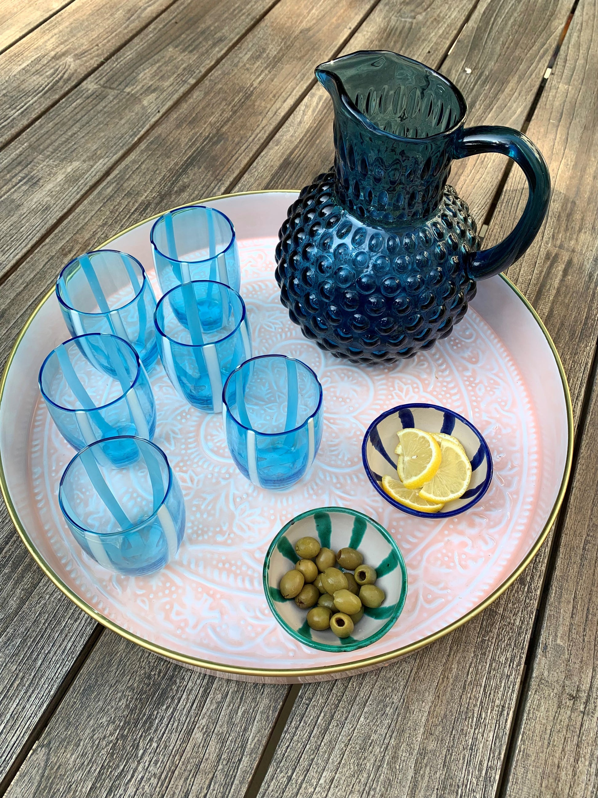 A large pink embossed tray with some blue tumblers, a blue jug and some olives.