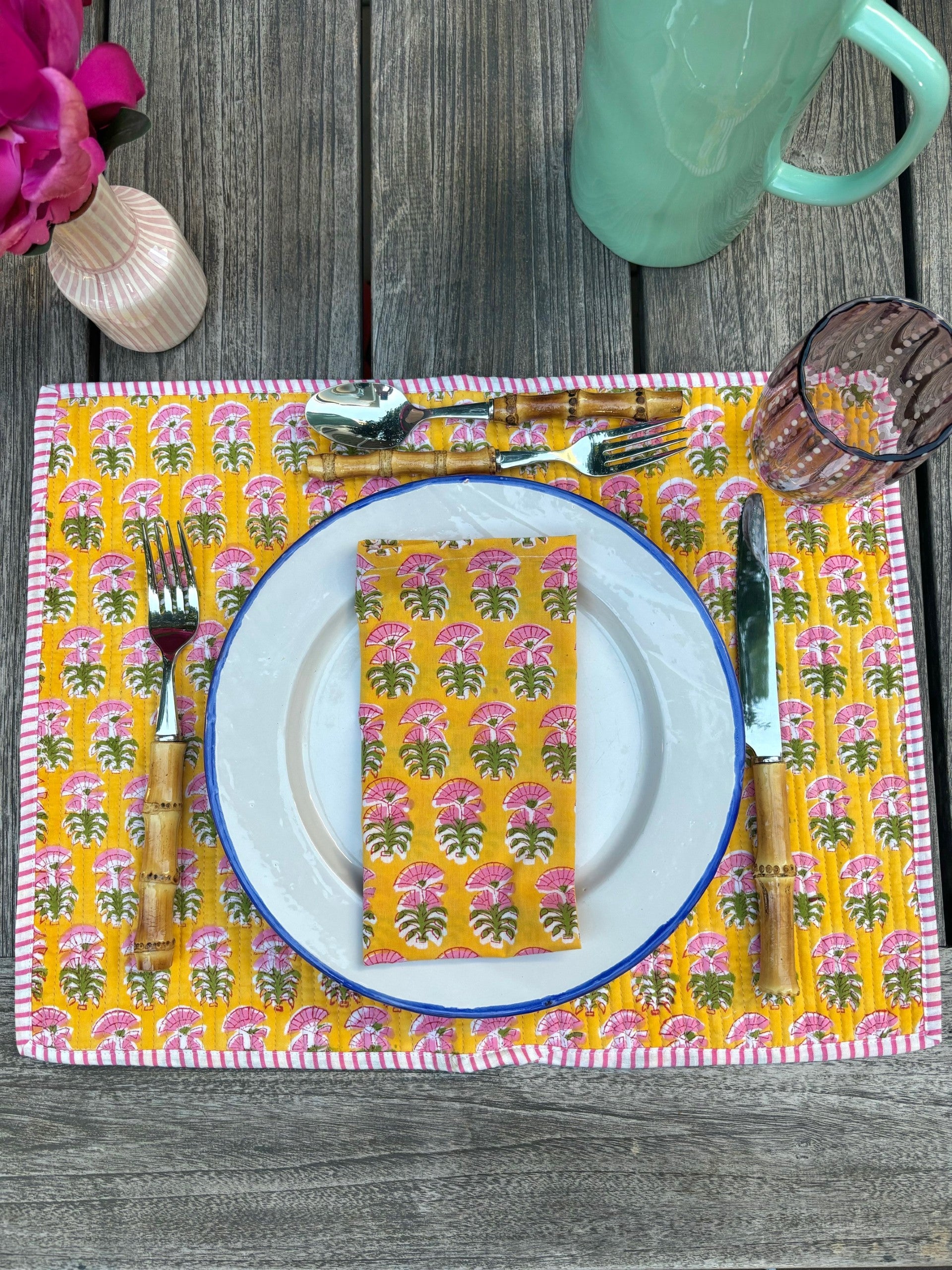 A table setting with a matching yellow block printed placemat and napkin set with a pink flower design.