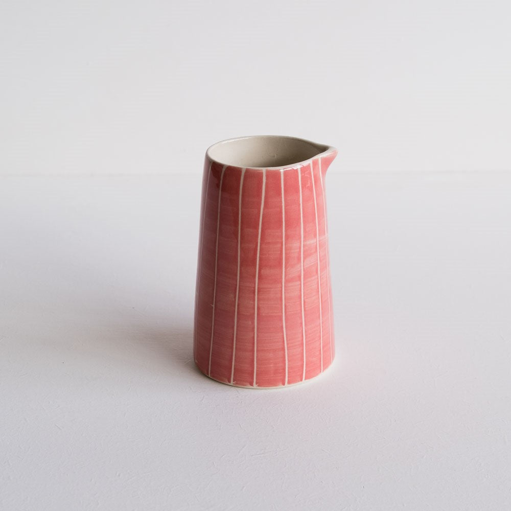 A rose pink creamer jug with hand-painted white stripes.