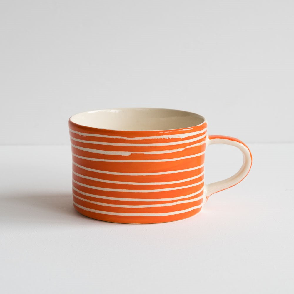 An orange hand-painted wide squat mug with white horizontal stripes