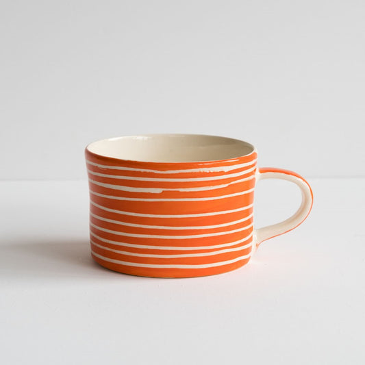 An orange hand-painted wide squat mug with white horizontal stripes