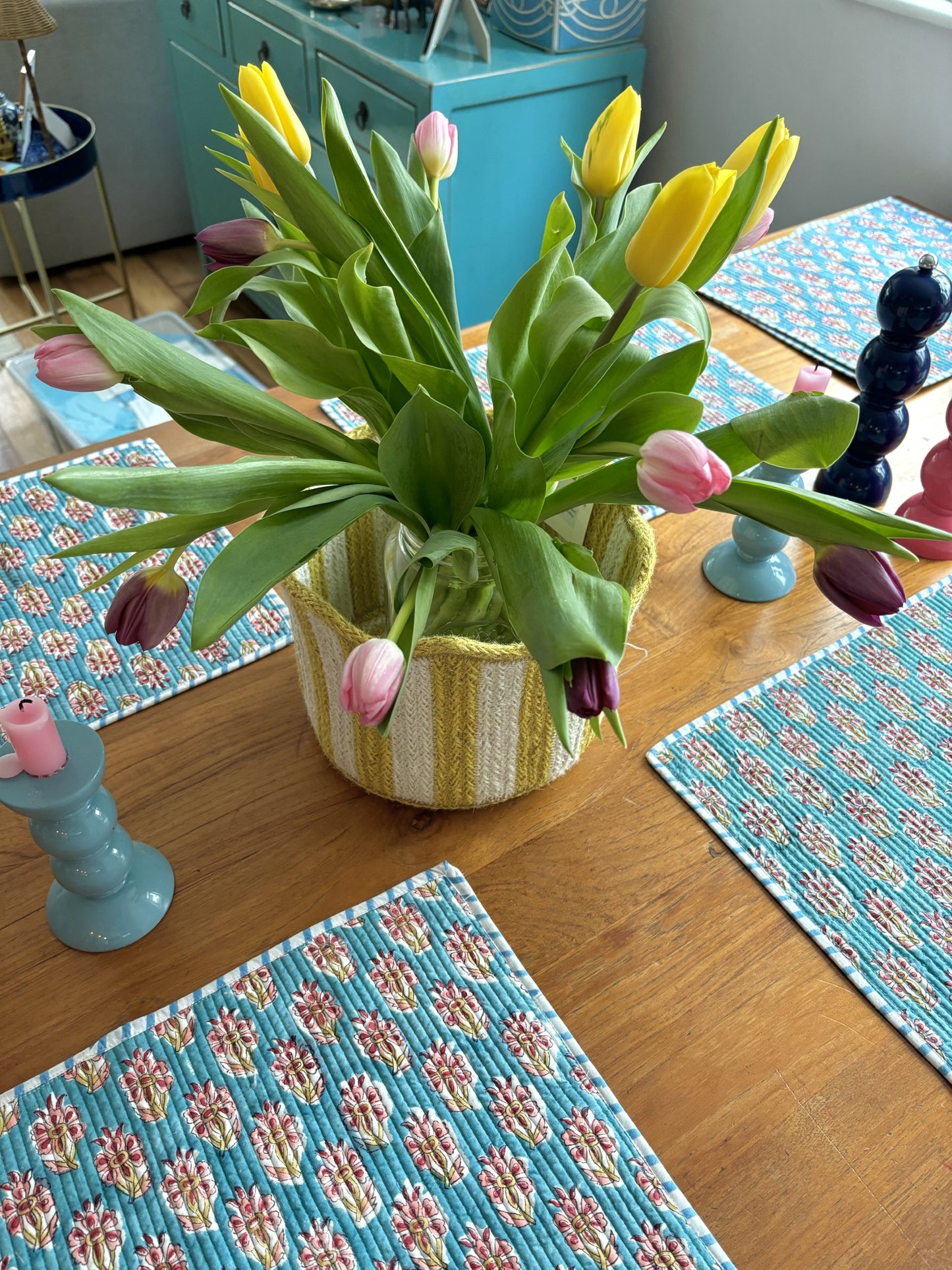 A yellow striped tulip basket filled with tulips on a dining table