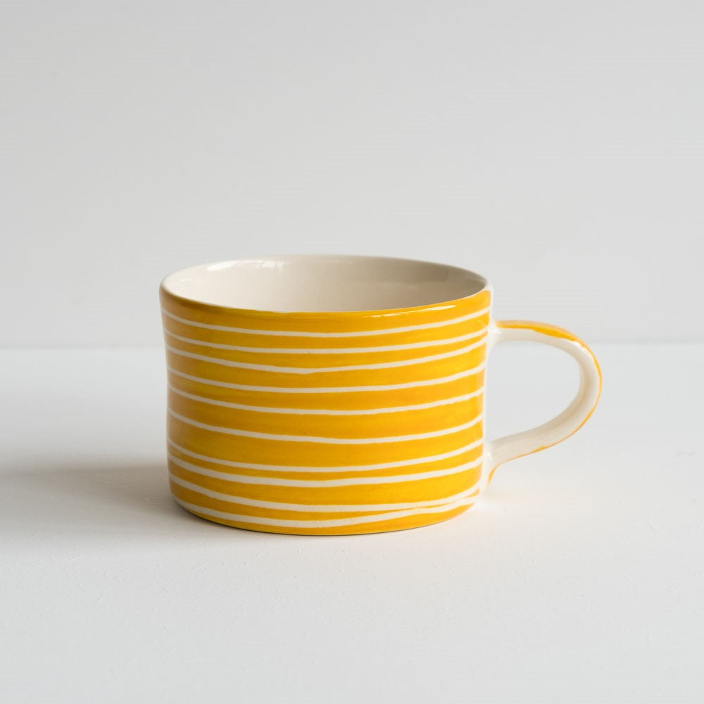 A yellow and white squat coffee mug from Musango with white horizontal sgraffito stripes.