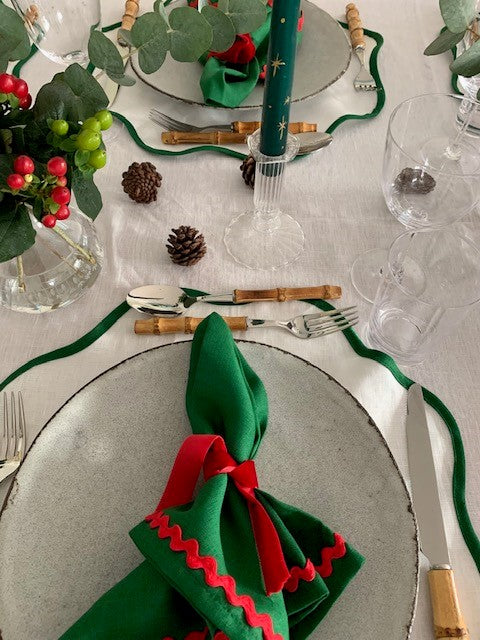 A Christmas place setting with a red, white and green colour scheme.  The cutlery has bamboo handles and is surrounding the plates on a white and green linen scallop placemat.