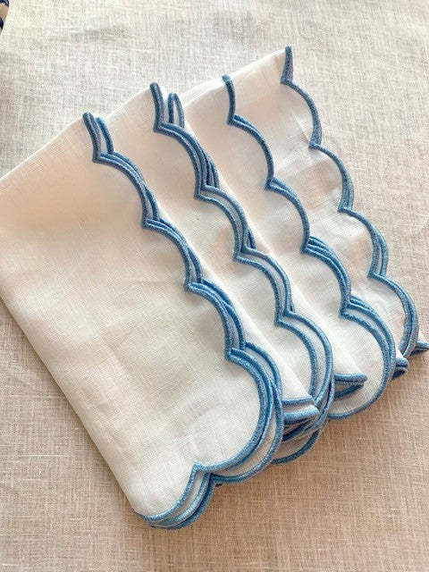 A set of 4 white linen napkins with a blue embroidered scalloped edge.