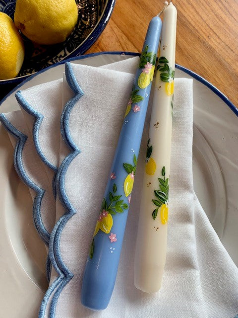 White linen napkins on a plate and topped with two hand-painted candles. There is a bowl of lemons on the table too.