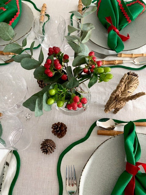 A christmas place setting with a crystal bud vase in the middle of the table filled with red and green berries.  The table linen is also red, green and white.