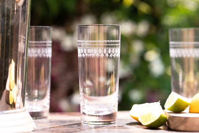 Three crystal highball glasses next to an ice bucket and some lemon wedges.  The highball glasses have been engraved with a delicate oval pattern.