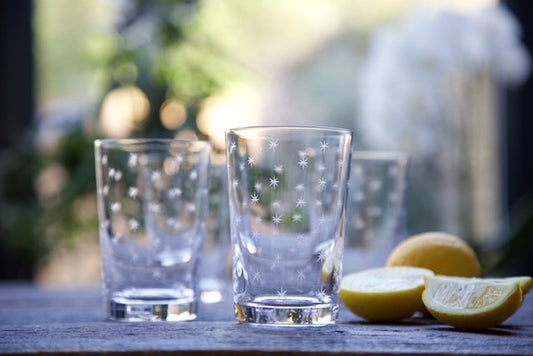 Crystal glass tumblers set on a table next to a cut lemon.  Each tumbler has a pattern of engraved stars.