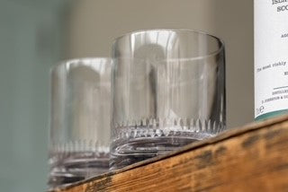 Two crystal whiskey glasses perched on a ledge.  Each whiskey glass has a spears pattern around the base rim.