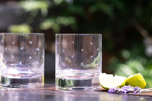 Two crystal whiskey glasses with hand-etched stars set on a table next to a lemon wedge.