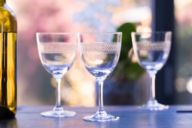 Three crystal wine glasses set on a table next to a wine bottle.  Each glass has been hand engraved with a latticed design.