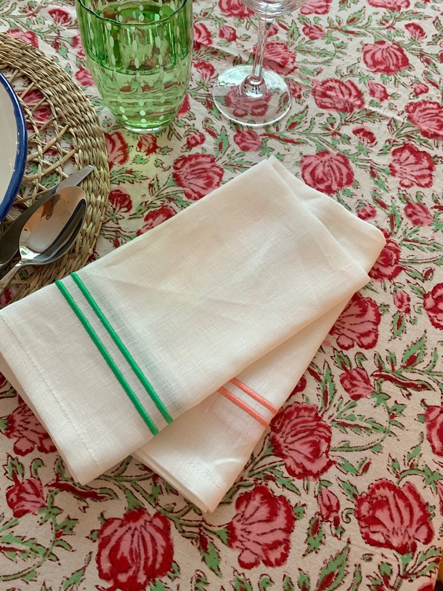 Some white linen napkins with green and pink piping on a green and pink floral block printed tablecloth.