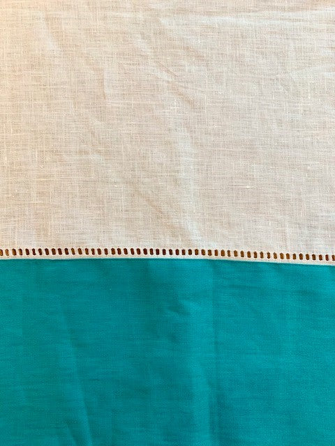A close up of a white linen tablecloth with a large teal border.