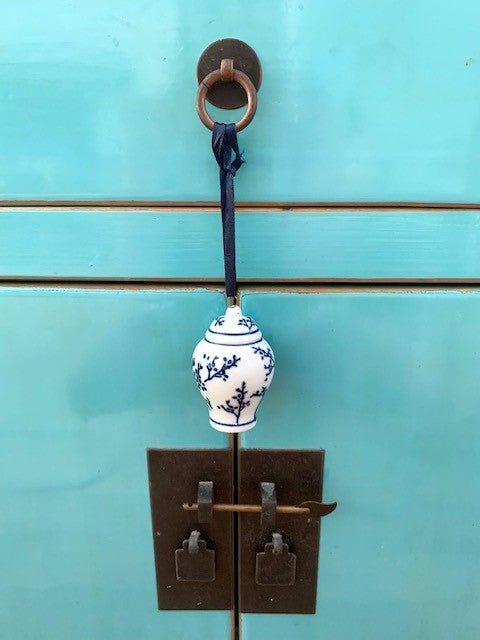 A mini blue and white ginger jar hanging from a blue chinese cabinet
