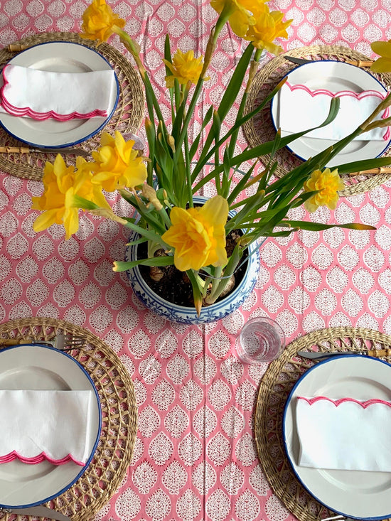 Birds eye view of daffodils set on a pink block printed tablecloth.  There are four plates laid alongside with pink edged scalloped napkins.