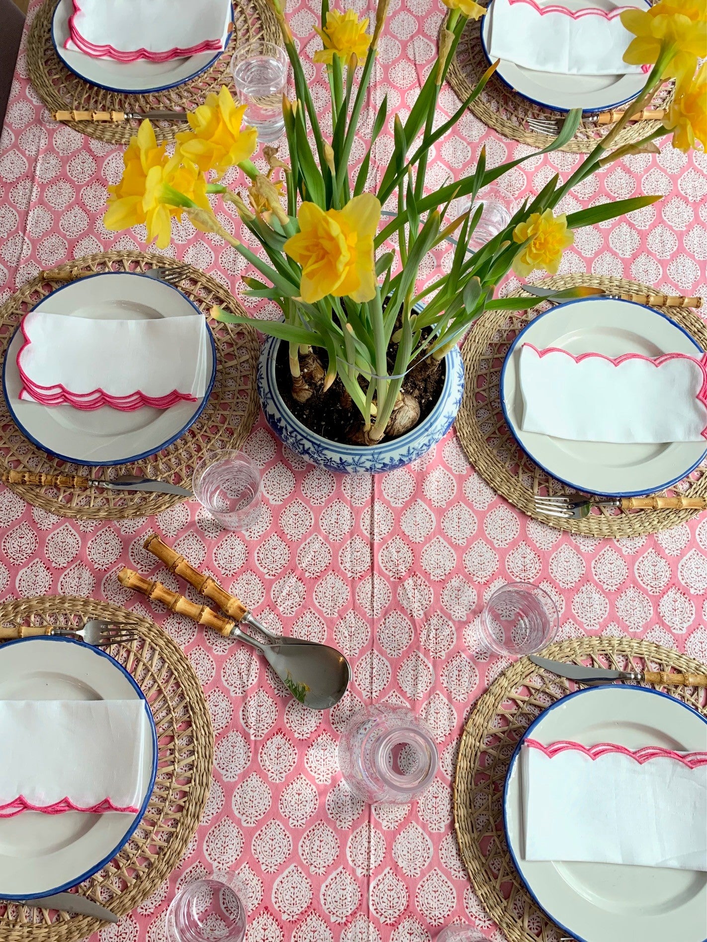 Birds eye view of a laid table with a pink block printed tablecloth and daffodils as the centre piece.