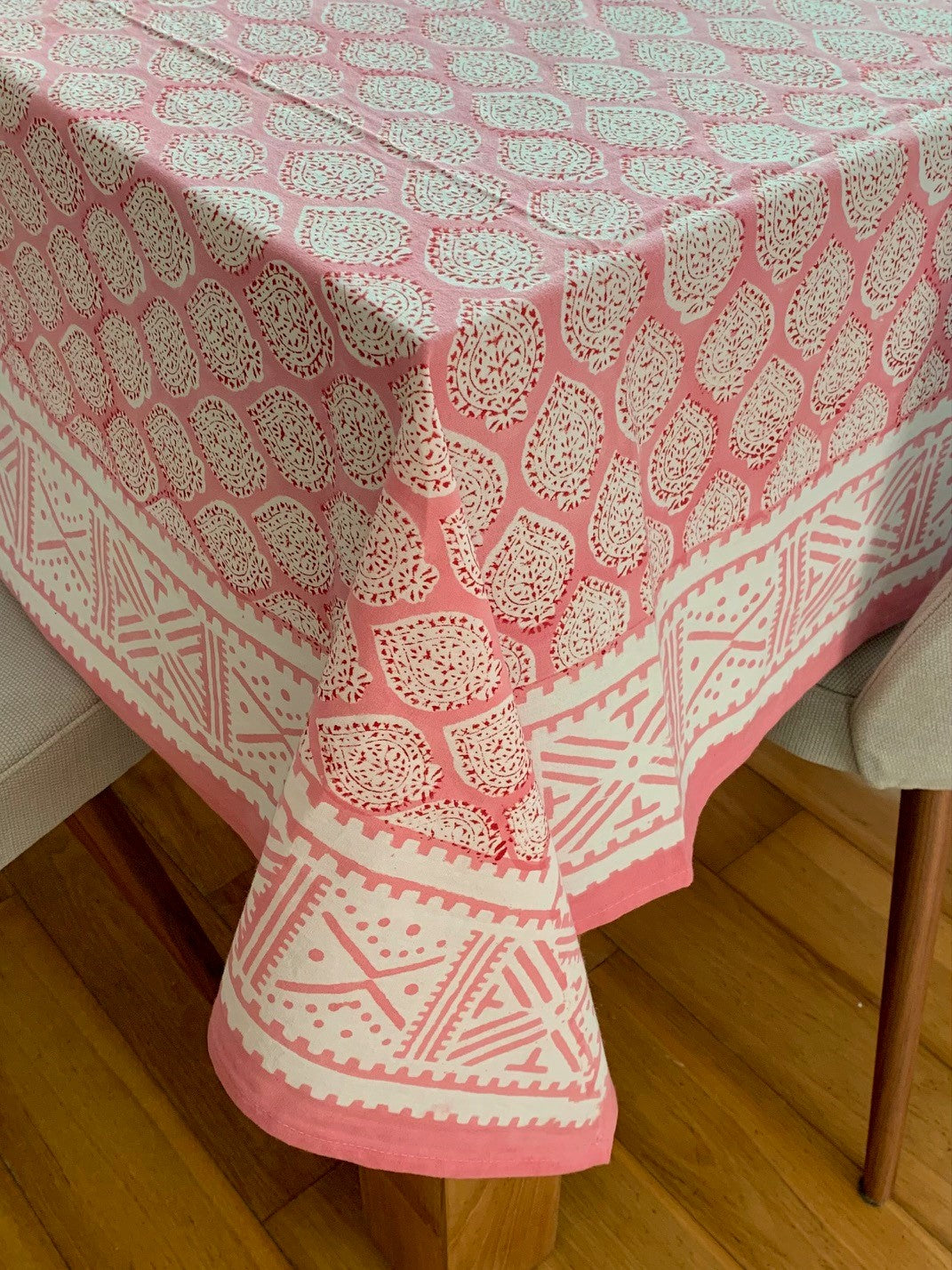 Pink block printed tablecloth with a leaf design and a border.