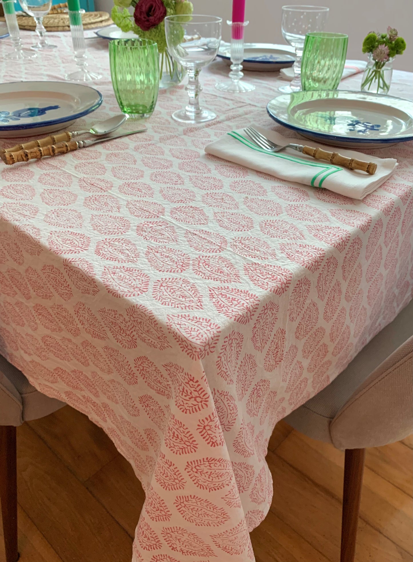 A pink block printed tablecloth laid with plates, wine glasses and green glass tumblers.