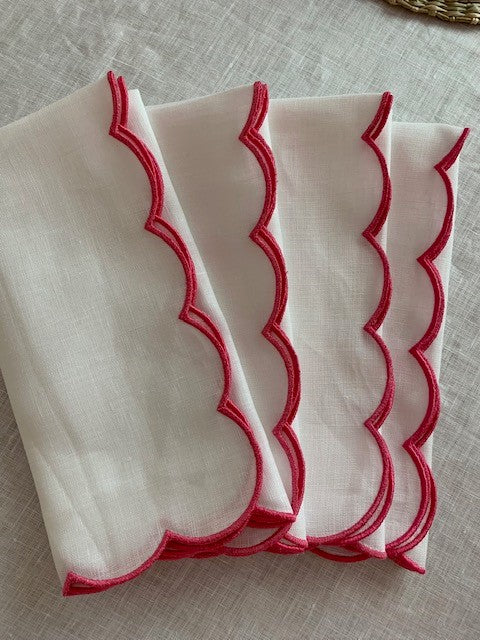 A set of 4 white linen napkins with an embroidered pink scalloped edge.