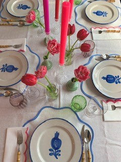 Valentines table setting with blue rimmed scallop placemats, pink tulips and bright pink and red candles